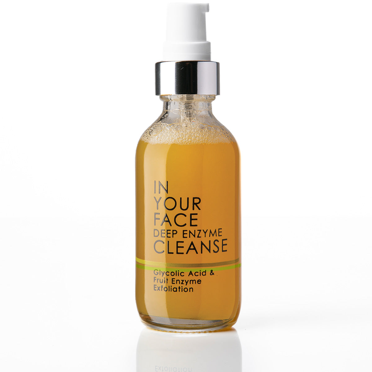 A clear glass bottle of IN YOUR FACE Deep Enzyme Cleanse with a white pump and silver collar, filled with an amber-colored liquid, on a white background with a soft reflection.