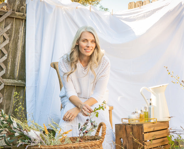 Pretty grey haired woman sits in front of white cloth next to skincare products