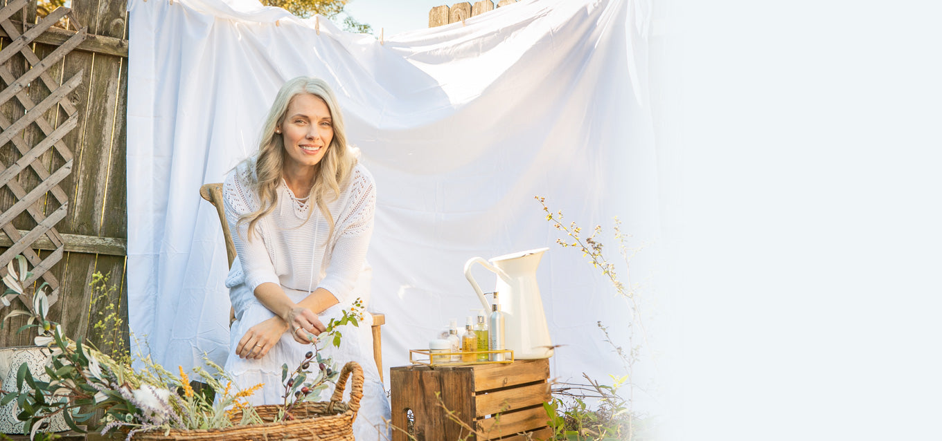 Pretty grey haired woman sits in front of white cloth next to skincare products