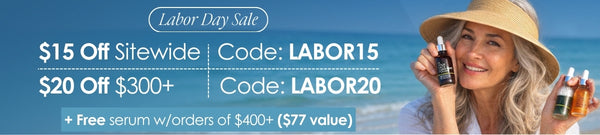 Labor Day sale promotional banner with text offering $15 off sitewide code LABOR15 and $20 off $300+ code LABOR20 plus a free serum with orders of $400+. A smiling woman in a straw hat holds two small serum bottles against a beach background.