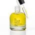 A clear glass bottle of In Your Face Nourishing Oil filled with yellow oil, shown with a black-capped dropper resting against the neck on a white background.
