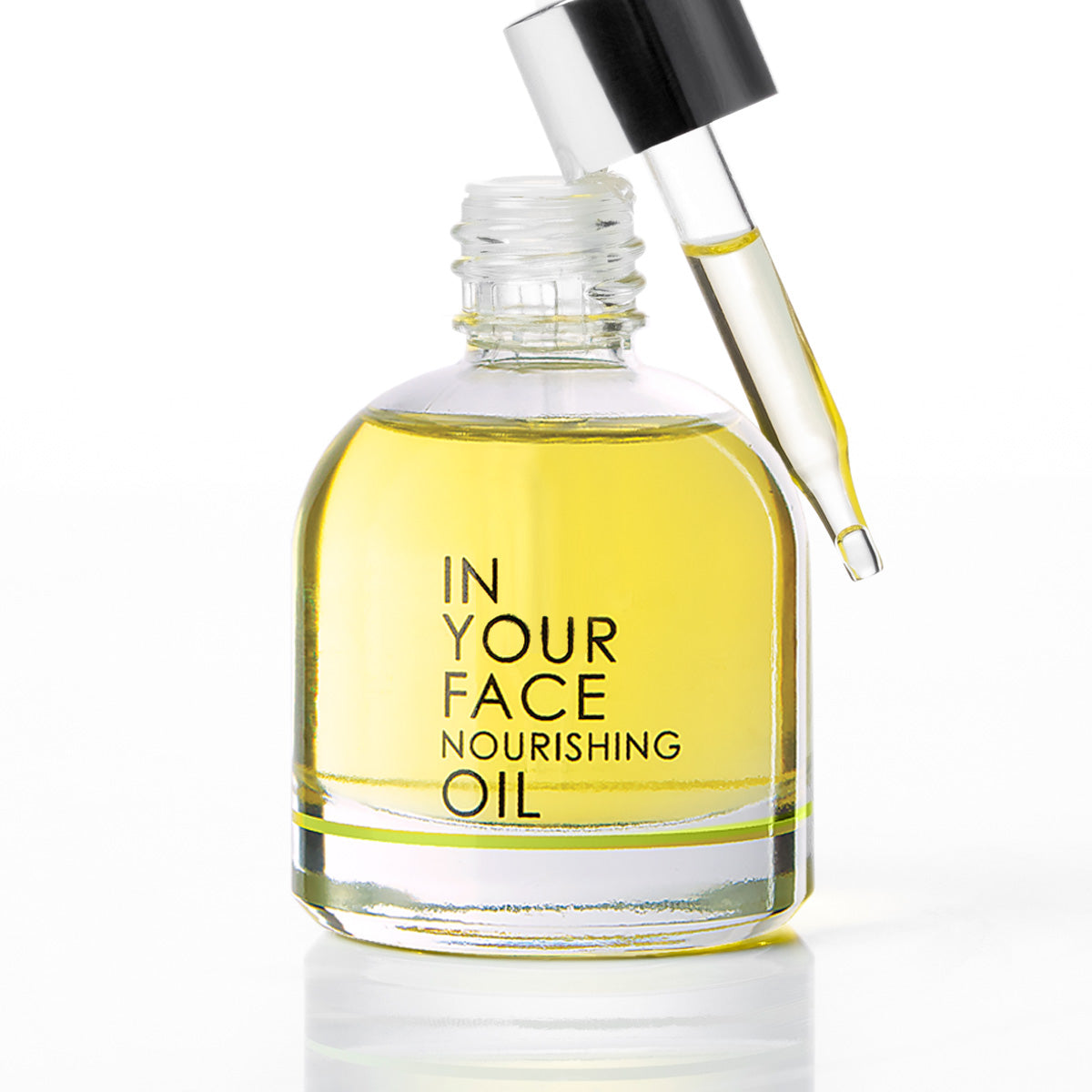 A clear glass dropper bottle of 'In Your Face Nourishing Oil' filled with golden yellow oil, featuring a black dropper with a clear glass pipette resting against the open bottle neck, set against a clean white background.