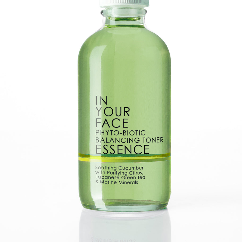 A clear glass bottle of IN YOUR FACE Phyto-Biotic Balancing Toner Essence, filled with a light green liquid and featuring black text on a white background.