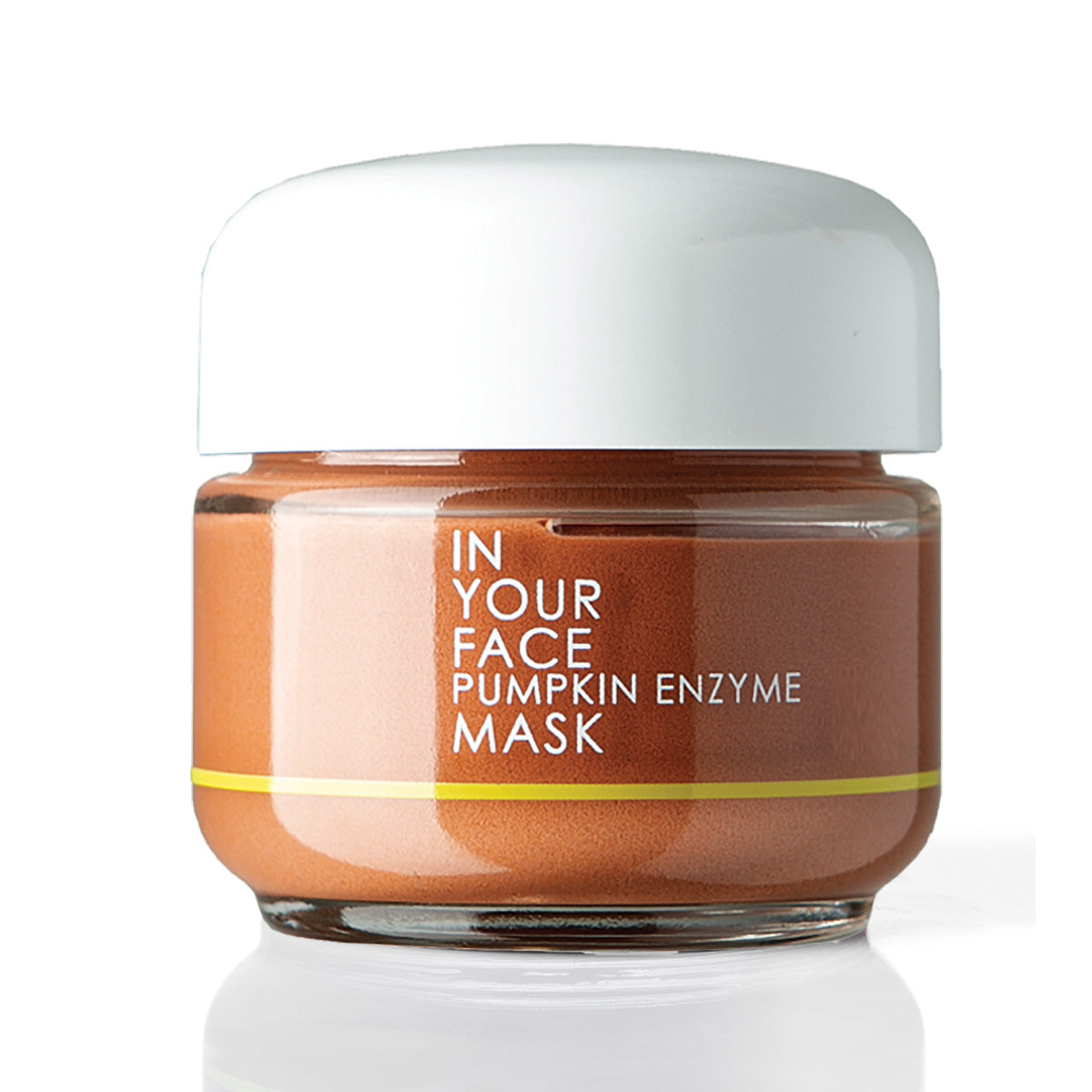 A jar of In Your Face Pumpkin Enzyme Mask with a white lid and a brownish-orange mask visible through the clear glass jar, set against a white background with a soft reflection.