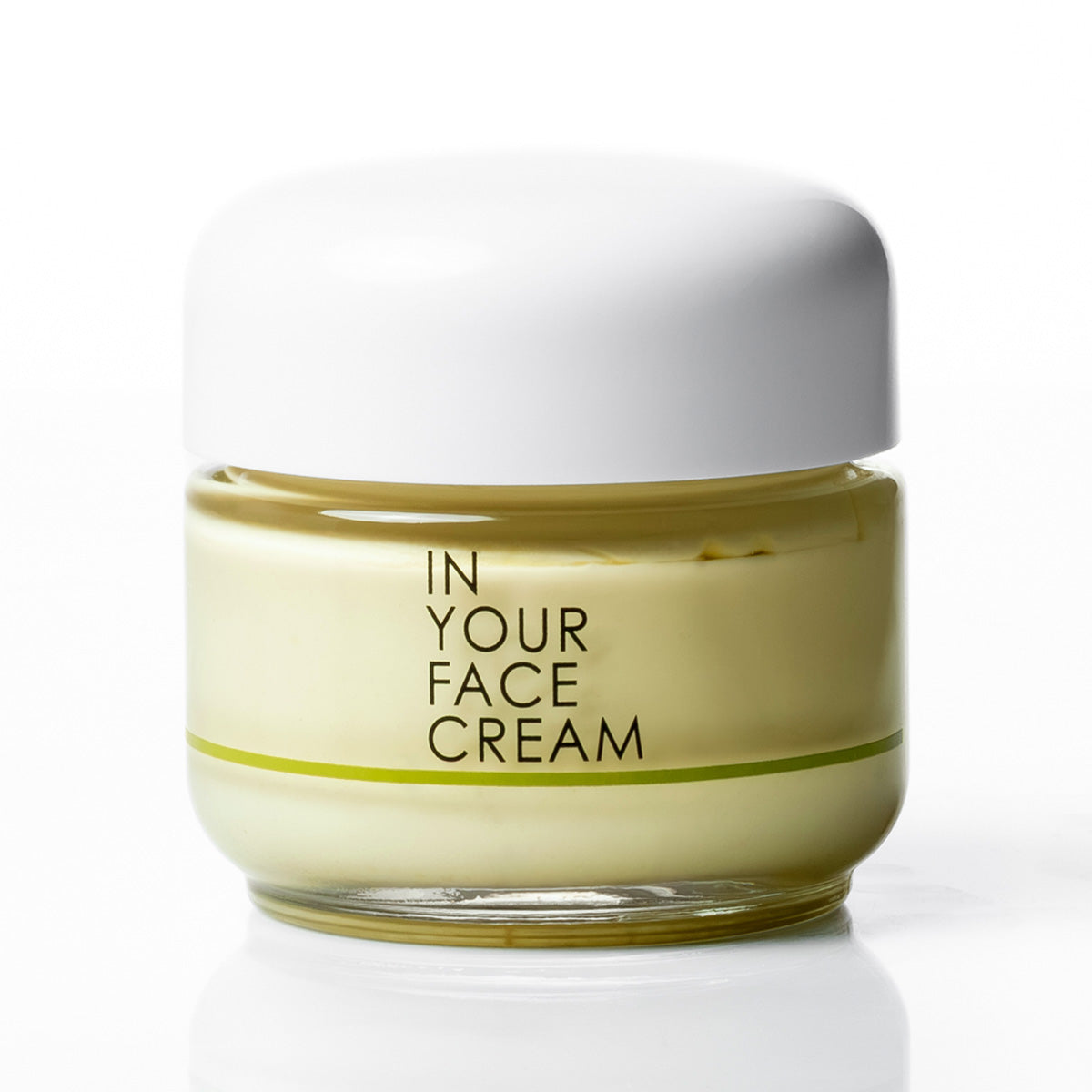 A jar of 'IN YOUR FACE CREAM' with pale yellow cream visible through a clear glass container, topped with a white lid, set against a clean white background.