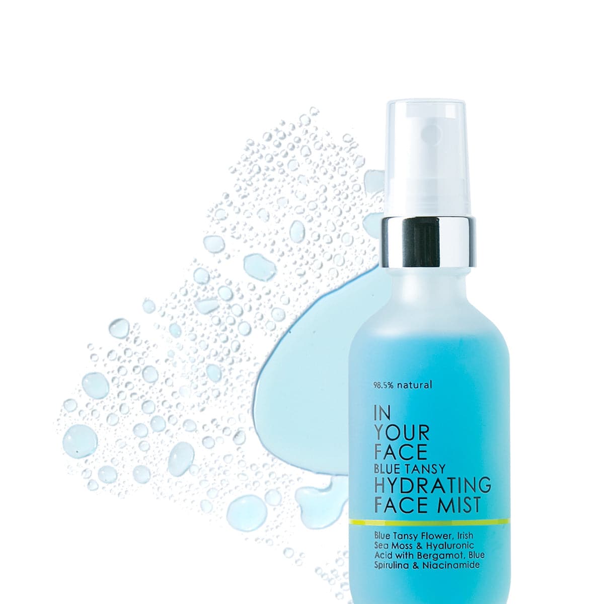 A bottle of the "98.5% natural IN YOUR FACE BLUE TANSY HYDRATING FACE MIST" on a white background. The bottle is clear but slightly frosted and is a bright blue color. The bottle also saying "Blue Tansy Flower, Irish Sea Moss & Hyaluronic Acid with Bergamot, Blue Spirulina and Niacinamide". Also is a splash of the toner on the side of the bottle showing the texture - liquid blue toner.
