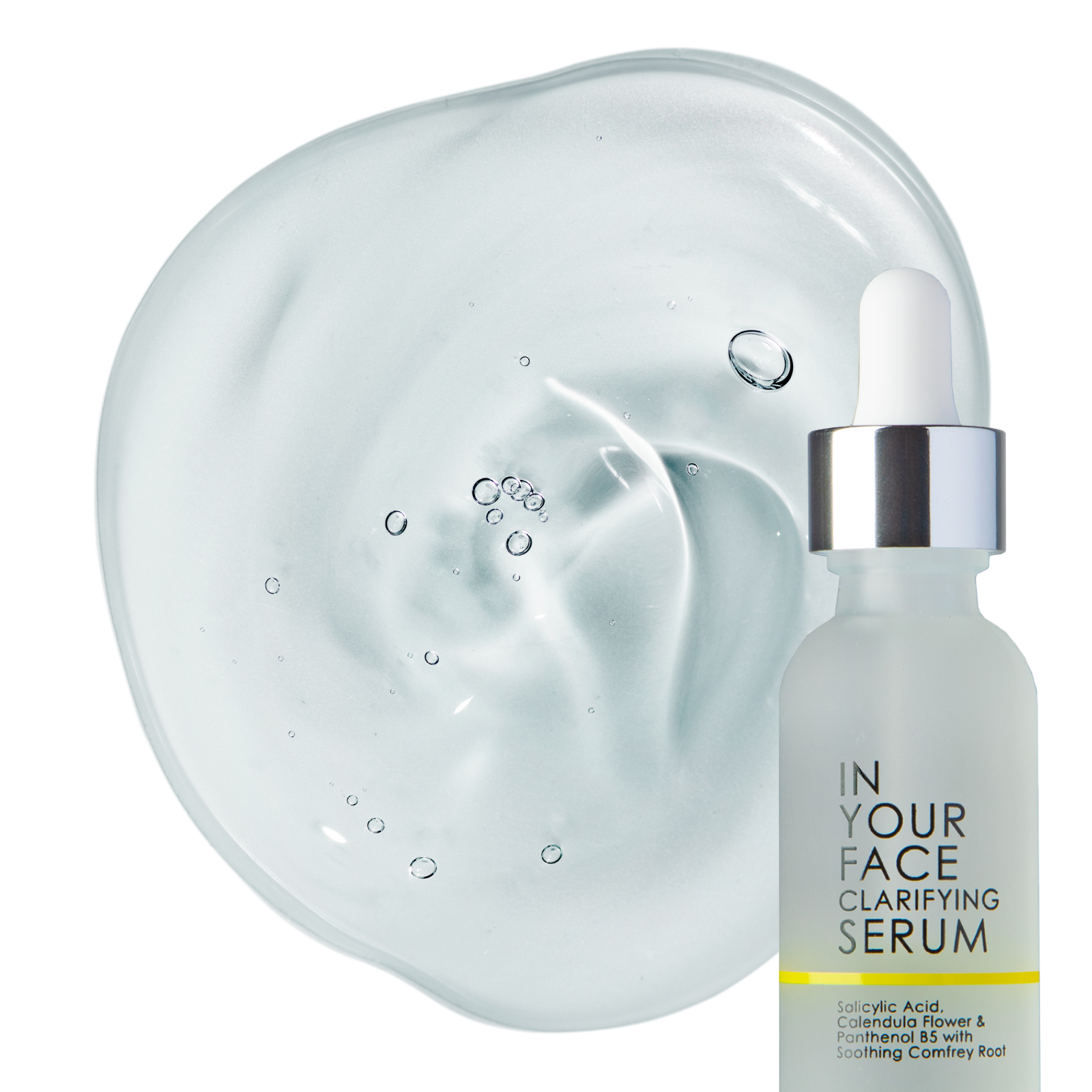 a bottle of the IN YOUR FACE CLARIFYING SERUM on a white background with a small shadow underneath the bottle. It shows a pipette that you can squeeze as the dispenser for the product on top. Next to the bottle you can see a clear dollop of the serum, which looks to be a medium thickness and a few bubbles on it.
