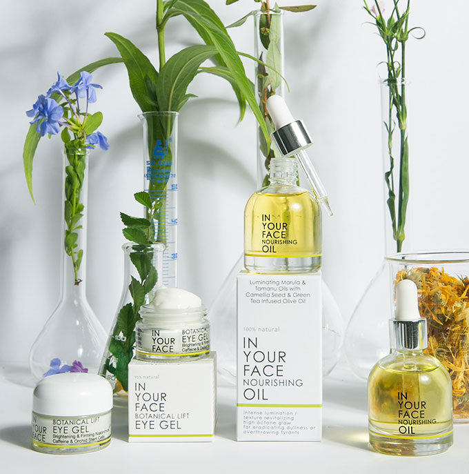 an image of beakers with botanicals inside beside a couple jars IN YOUR FACE BOTANICAL LIFT EYE GELs and a couple bottles of IN YOUR FACE NOURISHING OIL