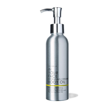 A metal bottle with a spout pump of the IN YOUR FACE HYDRATING CREAMY BODY OIL, saying "100% natural", with the words "Healing Calendula & Jojoba Oils, Satin-Soft Cocoa & Shea Butters with Revitalizing Citrus Oils"