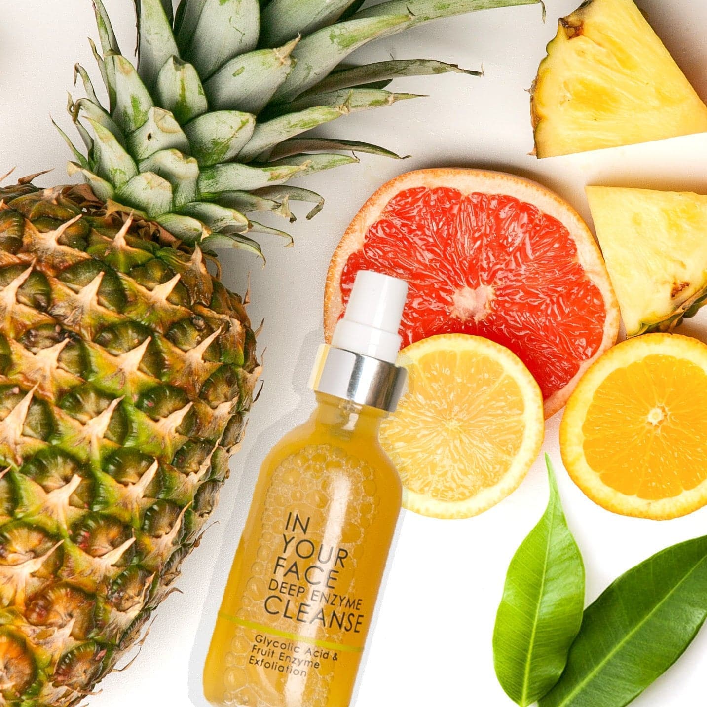a bottle of the DEEP ENZYME CLEANSE on a flatlay among a pineapple and citrus.