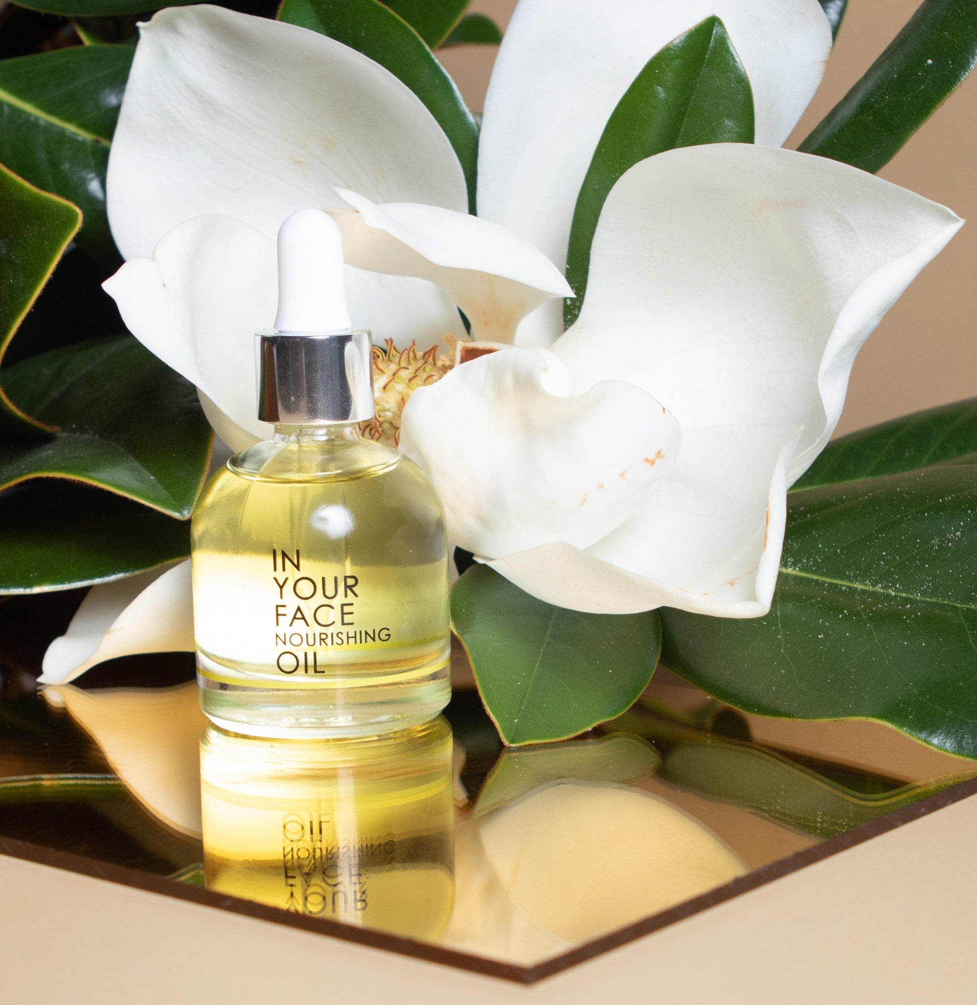 our nourishing oil in front of a magnolia flower on a beige background