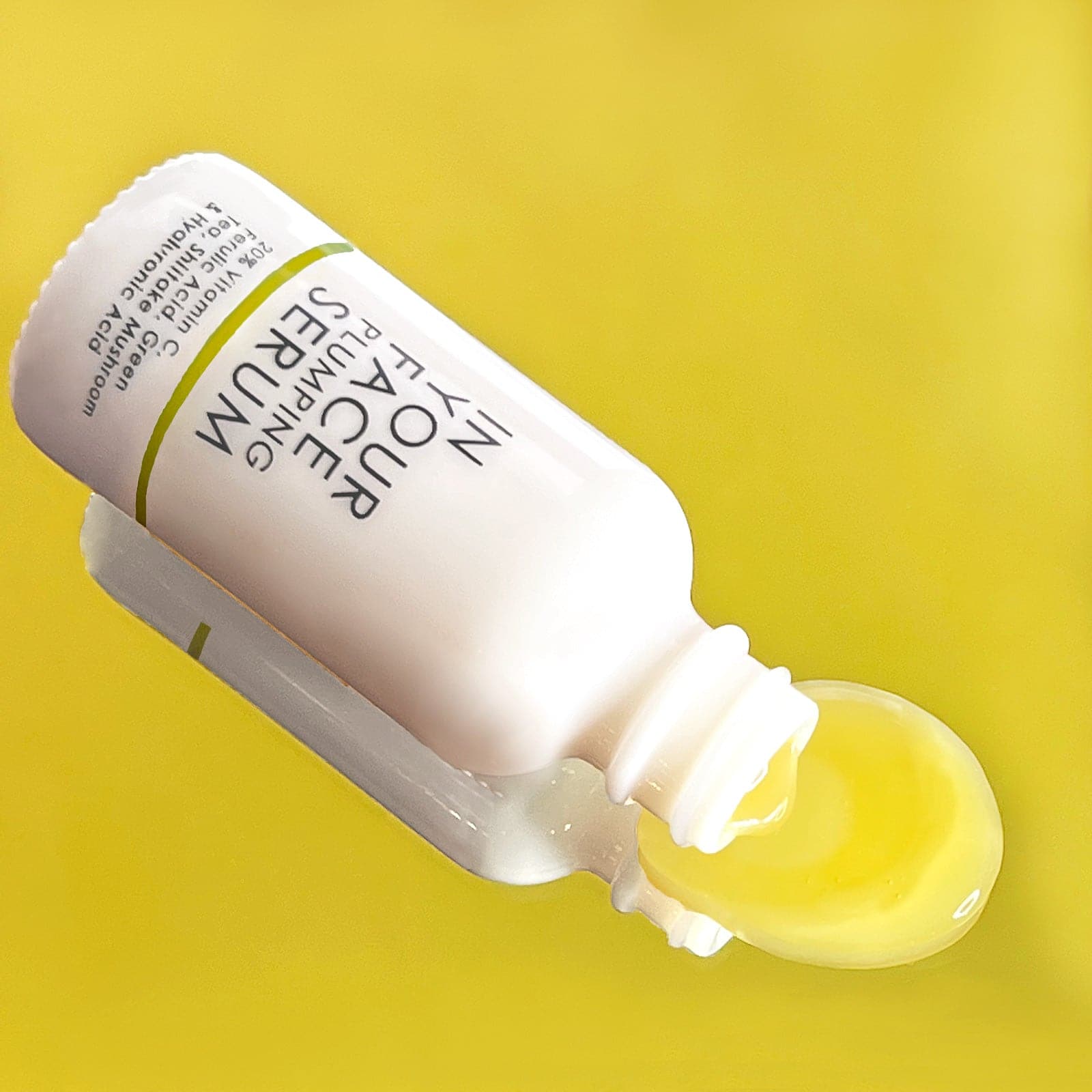 our VITAMIN C PLUMPING SERUM on a bright yellow background. The bottle is tipped over and some of the serum is coming out, a pale yellow color.