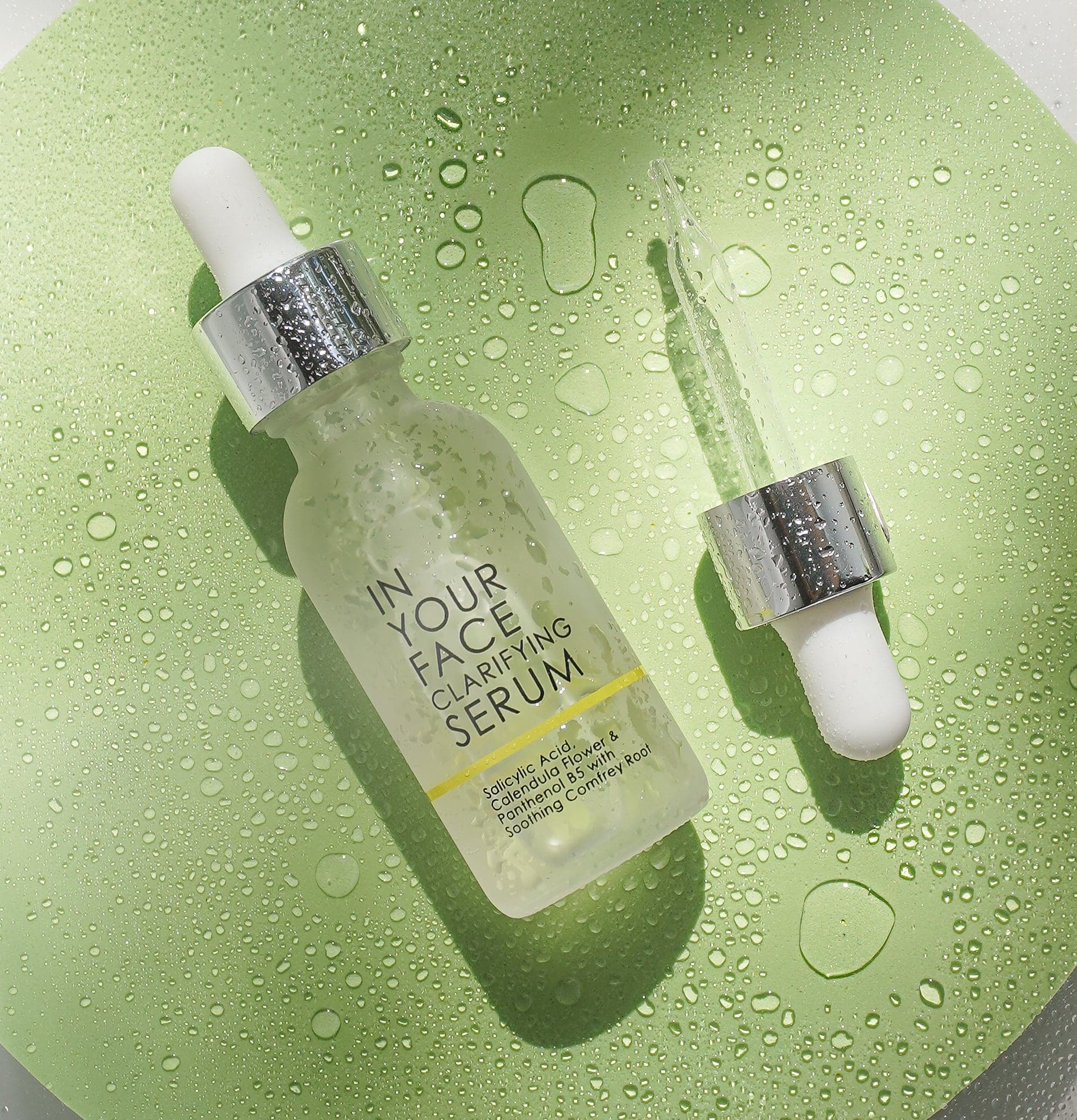 a bottle of the clarifying serum is laying on a dewy green surface, and next to it is a pipette.