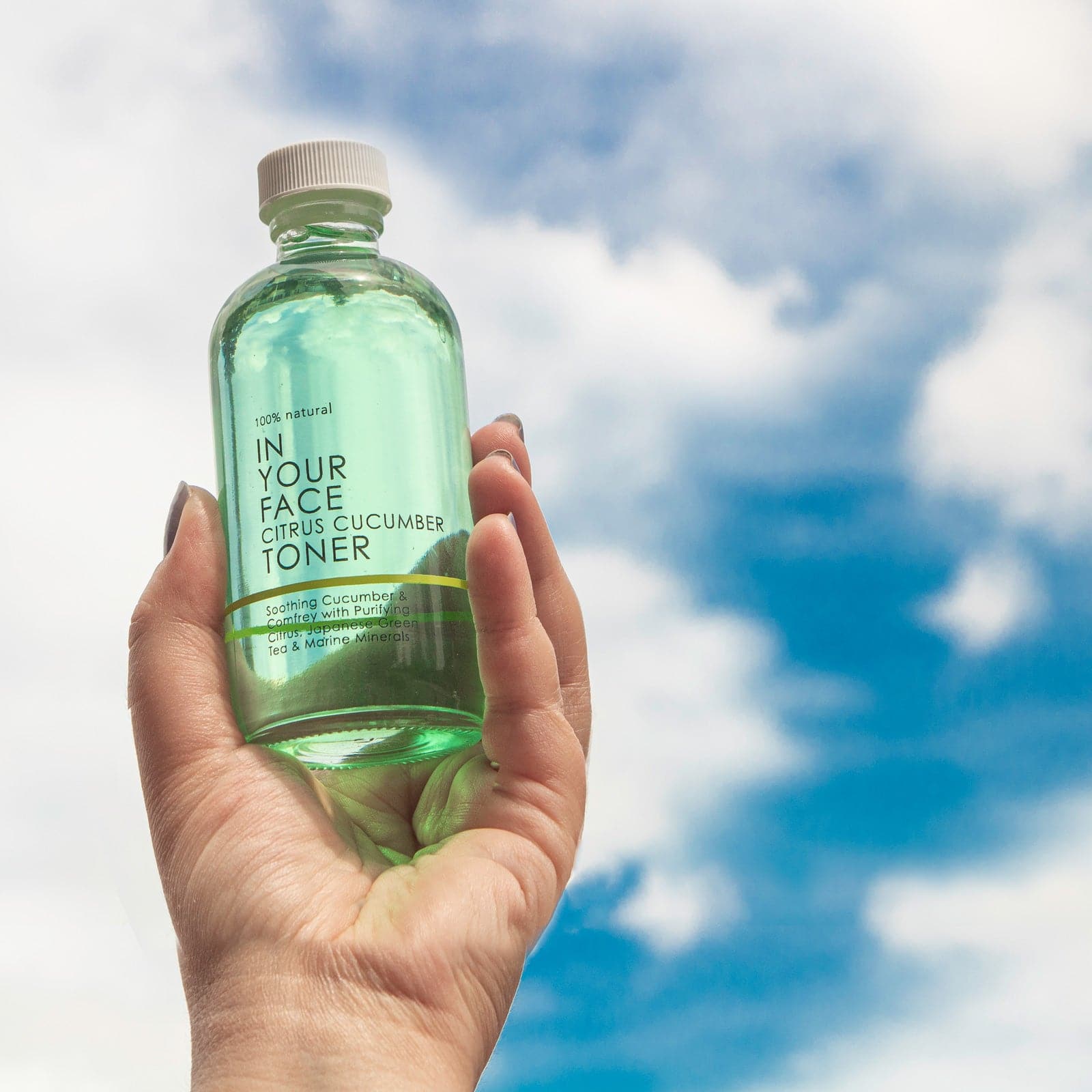 A bottle of the TONER being held in a hand up to a pretty blue sky with clouds.
