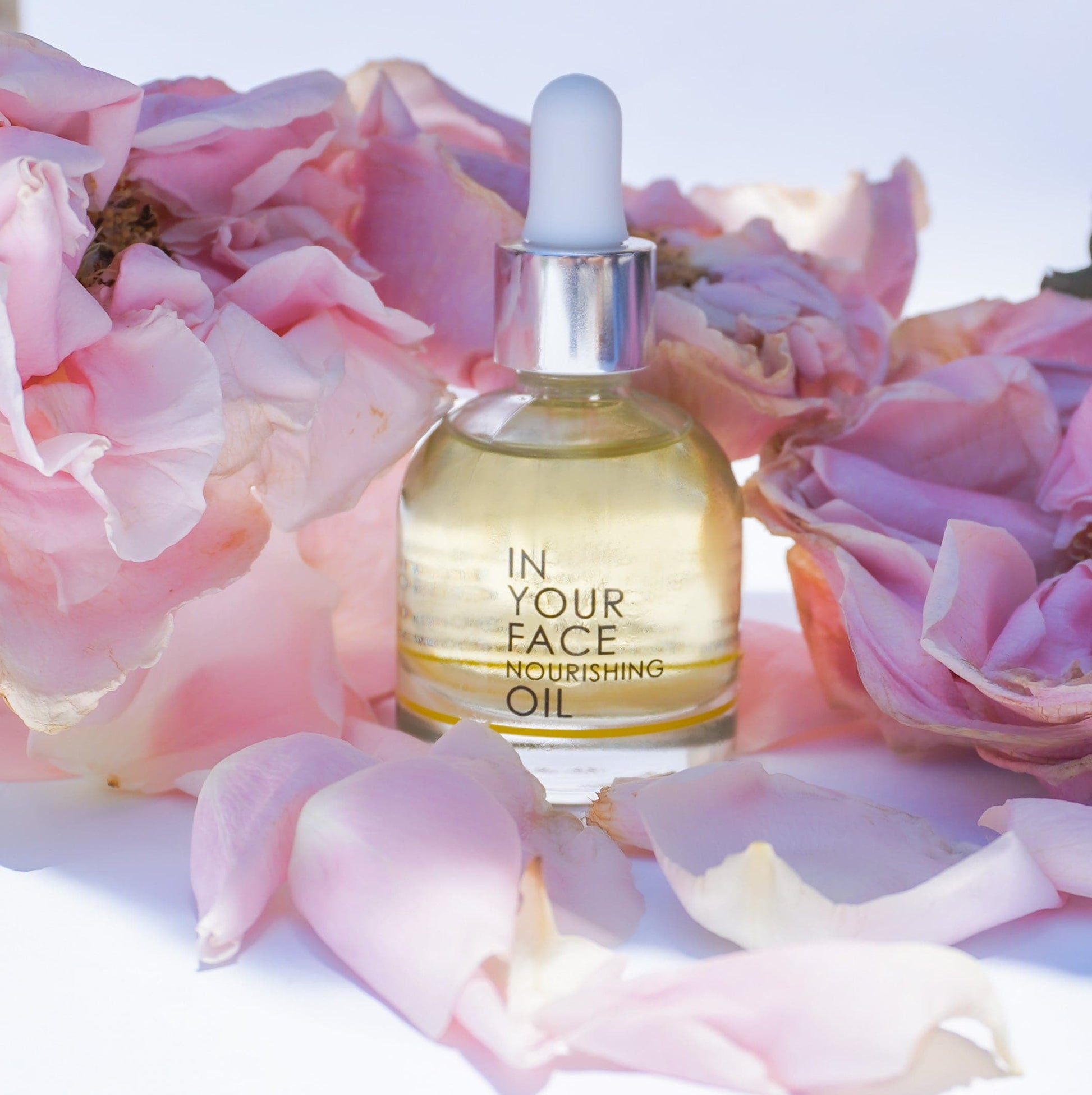 our nourishing oil among some peony petals on a white background